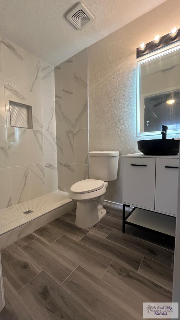 bathroom featuring a tile shower, vanity, a textured ceiling, and toilet