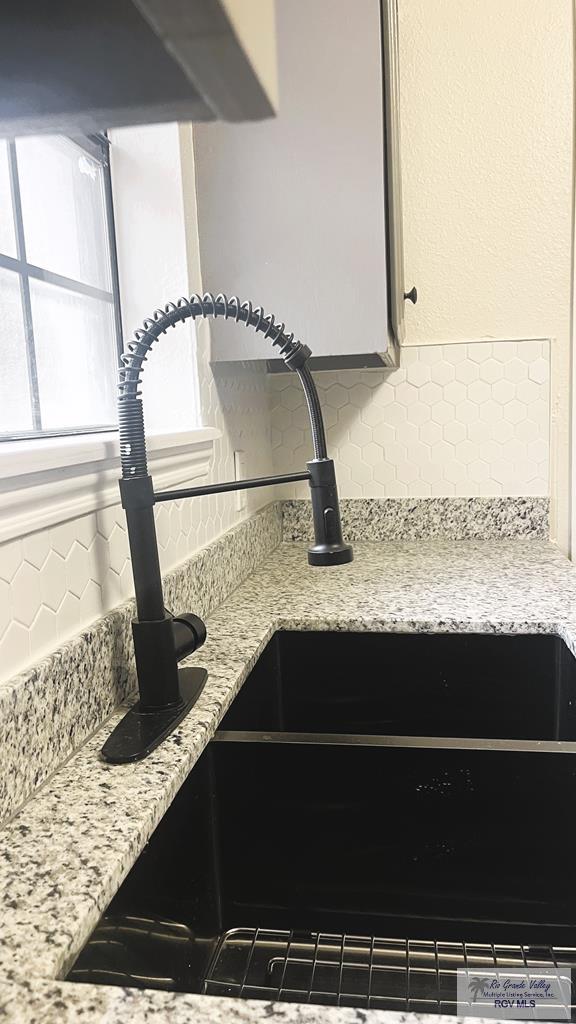 interior details featuring decorative backsplash, light stone countertops, and sink