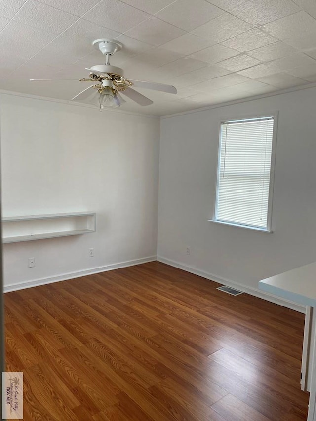 empty room with ceiling fan, wood finished floors, visible vents, and ornamental molding