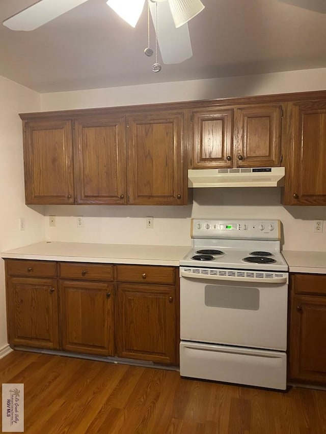 kitchen with brown cabinets, white electric range, under cabinet range hood, dark wood-style floors, and light countertops