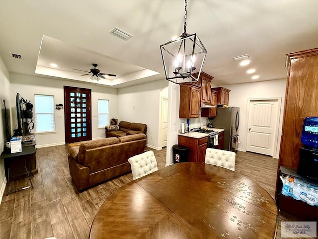 dining room featuring ceiling fan with notable chandelier, dark wood-type flooring, and a tray ceiling