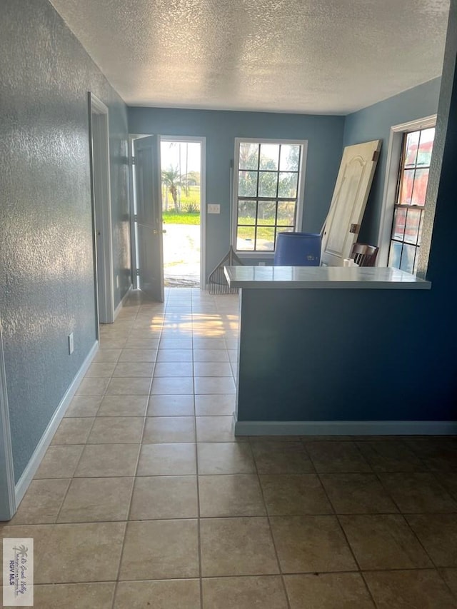 foyer entrance featuring light tile patterned floors, baseboards, a textured ceiling, and a textured wall