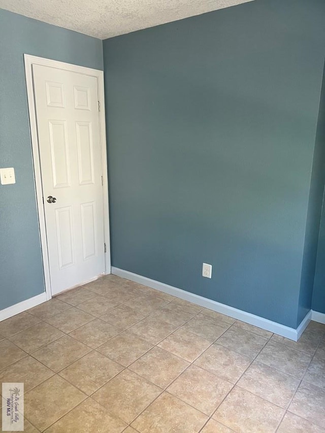 empty room featuring baseboards, a textured ceiling, and light tile patterned flooring