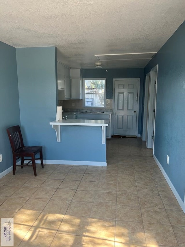 kitchen featuring light tile patterned flooring, a peninsula, a breakfast bar, white cabinets, and light countertops