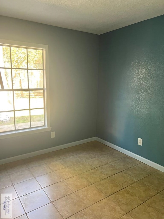 empty room featuring light tile patterned floors, baseboards, and a textured ceiling