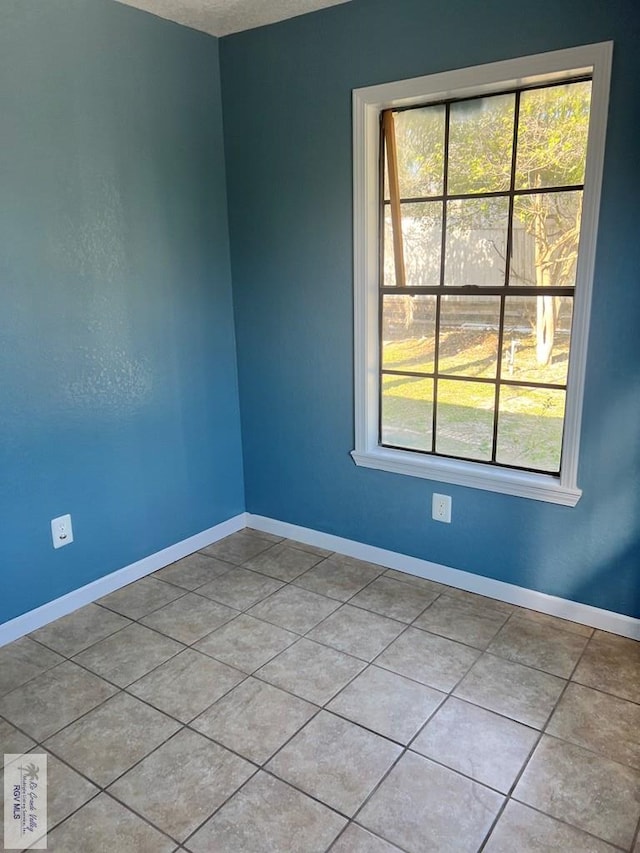 empty room featuring light tile patterned floors, baseboards, and a wealth of natural light