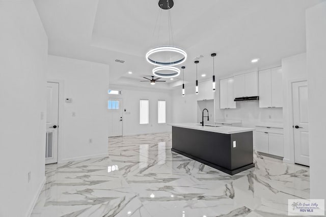 kitchen featuring sink, white cabinetry, hanging light fixtures, a center island with sink, and a tray ceiling