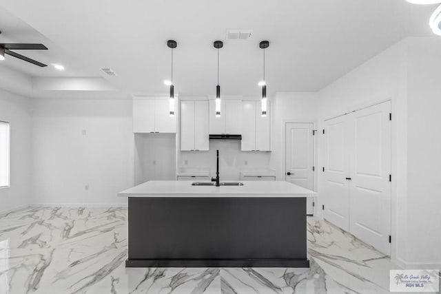 kitchen with an island with sink, sink, pendant lighting, and white cabinets