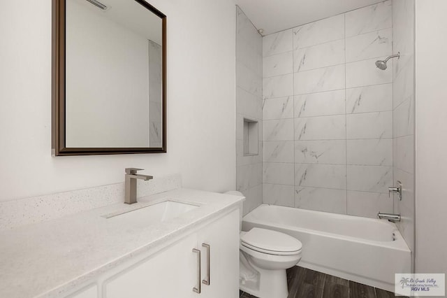 full bathroom with hardwood / wood-style floors, vanity, tiled shower / bath combo, and toilet