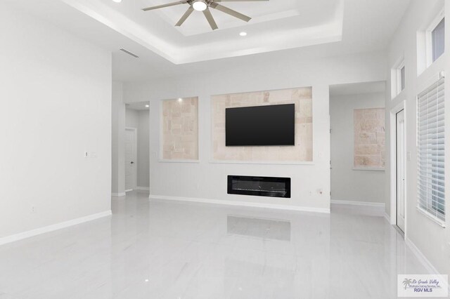 tiled living room with ceiling fan and a tray ceiling