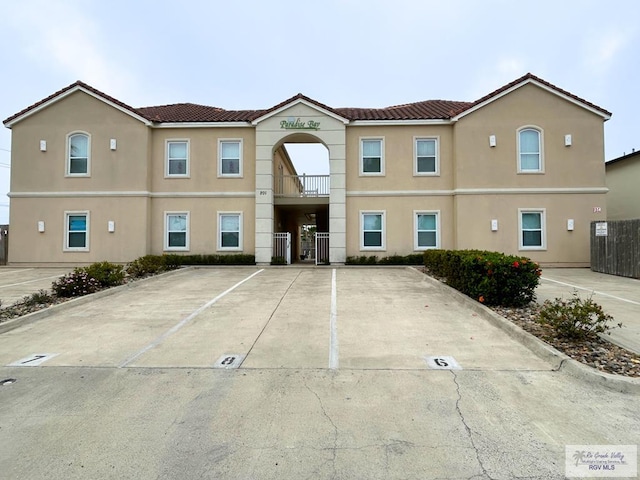 multi unit property with stucco siding, a tile roof, and uncovered parking