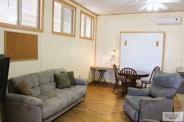 living room with a wall mounted AC, a wealth of natural light, ceiling fan, and light wood-type flooring