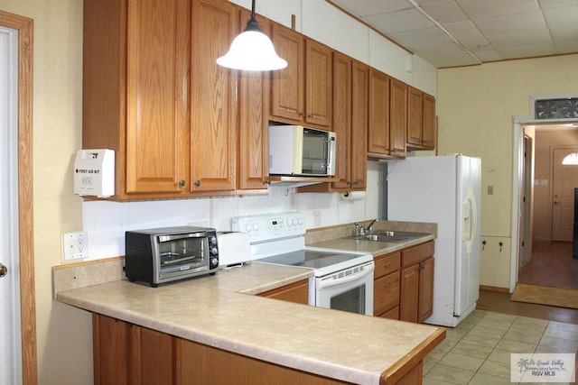 kitchen with white appliances, sink, light wood-type flooring, decorative light fixtures, and kitchen peninsula