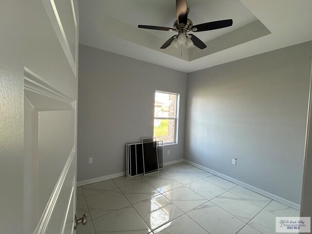 empty room featuring ceiling fan and a raised ceiling