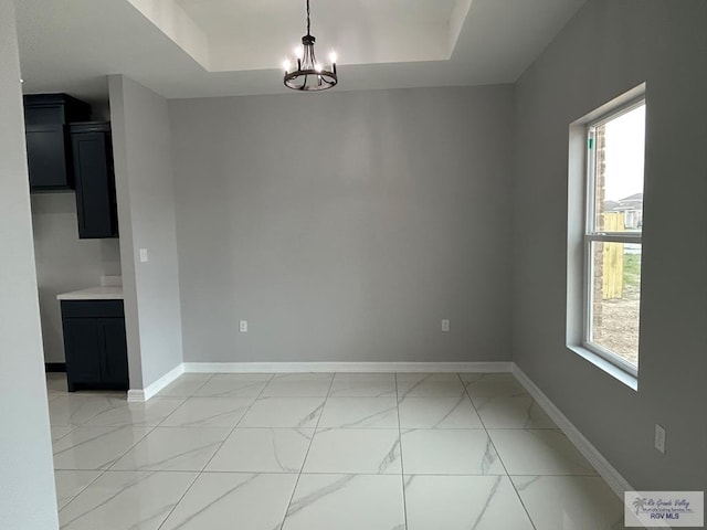 unfurnished dining area featuring a chandelier, marble finish floor, a raised ceiling, and baseboards