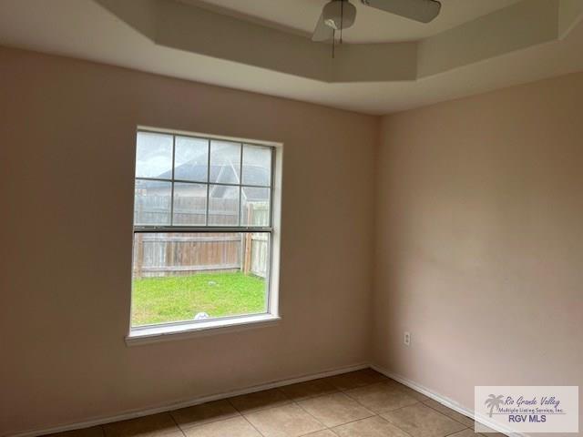 empty room with light tile patterned floors, a tray ceiling, a wealth of natural light, and ceiling fan