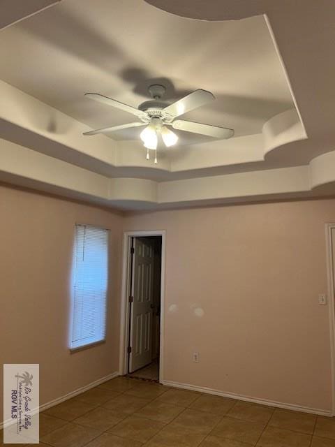 tiled empty room with a raised ceiling and ceiling fan