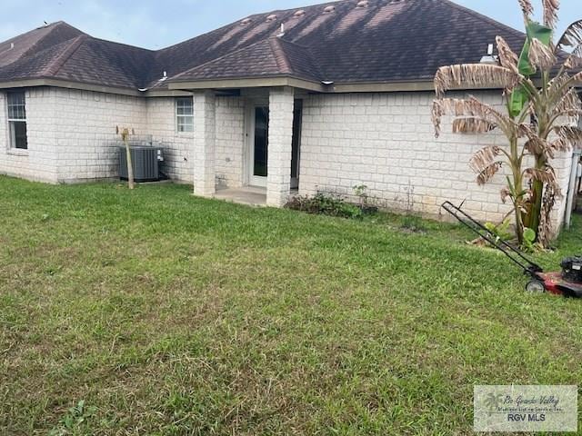 rear view of house featuring central AC unit and a lawn