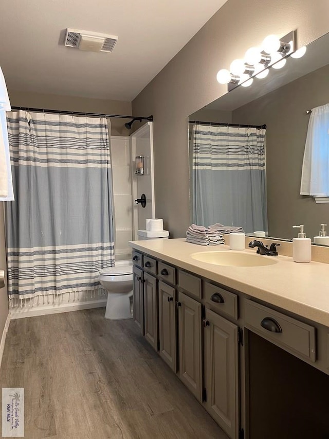 full bathroom with toilet, wood finished floors, vanity, visible vents, and shower / tub combo with curtain