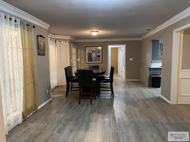 dining room featuring visible vents, baseboards, crown molding, and wood finished floors