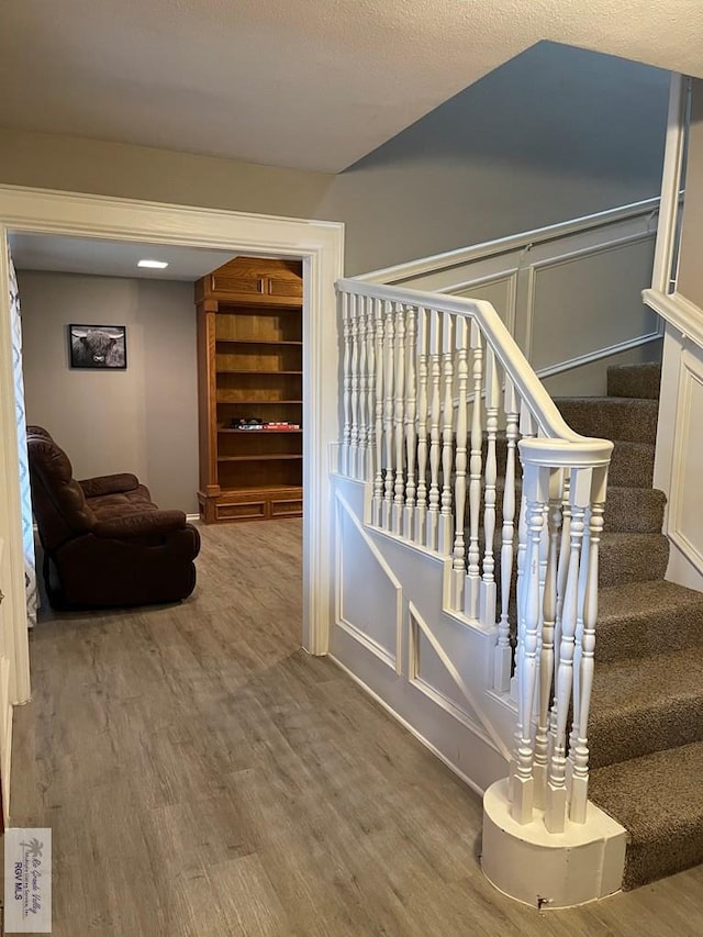 stairs featuring a decorative wall and wood finished floors