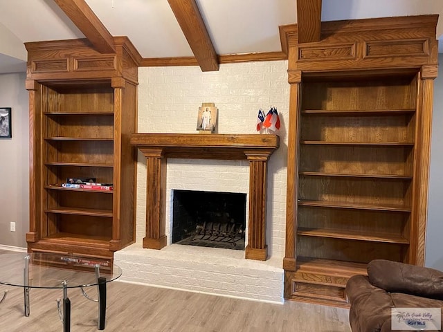 living area with beamed ceiling, a brick fireplace, and wood finished floors