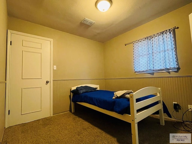 carpeted bedroom featuring wainscoting, visible vents, and wood walls