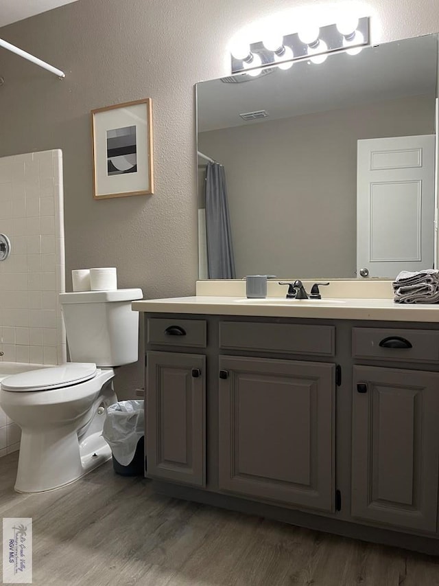 bathroom featuring visible vents, a textured wall, toilet, vanity, and wood finished floors