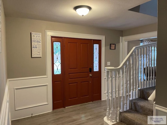 foyer entrance featuring a textured ceiling, stairway, wood finished floors, and a healthy amount of sunlight