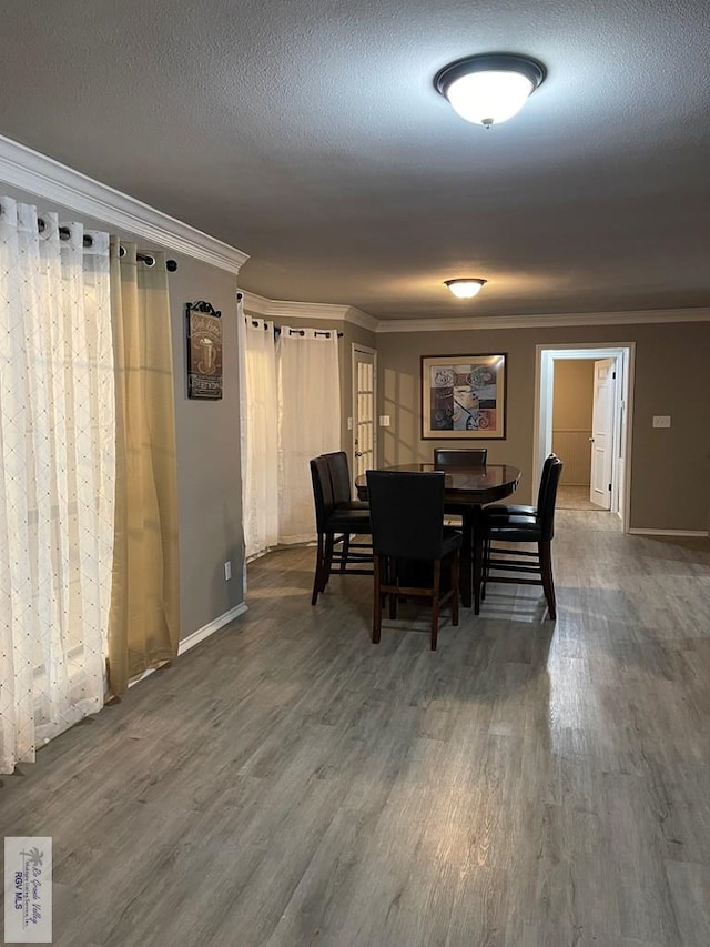 dining room featuring a textured ceiling, baseboards, wood finished floors, and crown molding