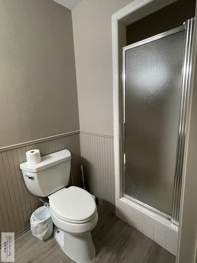 bathroom with a wainscoted wall, a stall shower, and wood finished floors