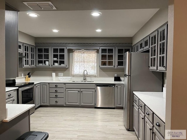 kitchen with stainless steel appliances, a sink, visible vents, gray cabinets, and glass insert cabinets