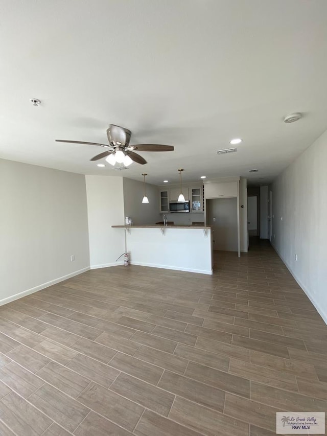 unfurnished living room featuring ceiling fan, sink, and hardwood / wood-style flooring