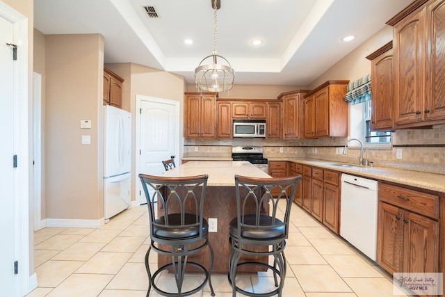 kitchen featuring a center island, sink, appliances with stainless steel finishes, a tray ceiling, and decorative light fixtures