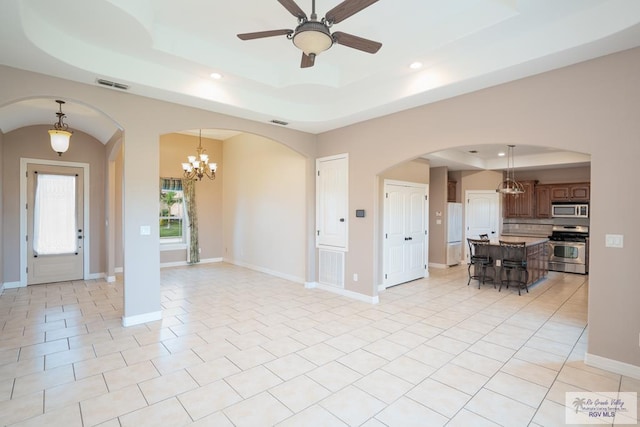 interior space with a tray ceiling and ceiling fan with notable chandelier