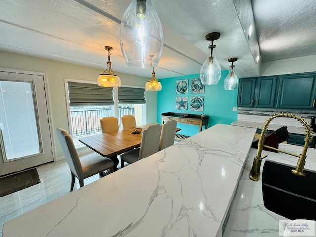 kitchen featuring light stone countertops, decorative backsplash, a textured ceiling, blue cabinets, and pendant lighting