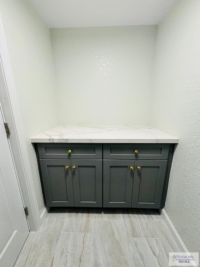 bar with gray cabinets and light stone counters