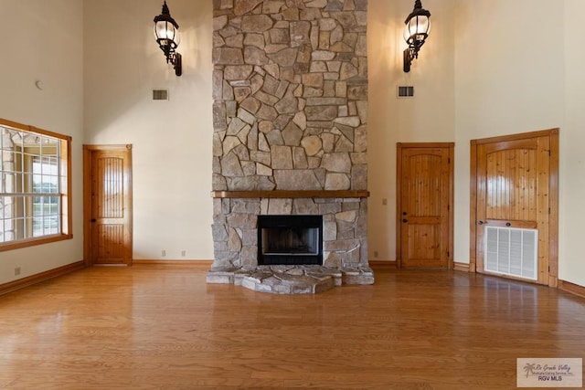 unfurnished living room featuring a stone fireplace, a towering ceiling, and wood-type flooring