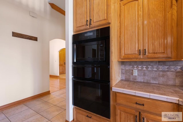 kitchen with tile counters, light tile patterned floors, black double oven, and tasteful backsplash