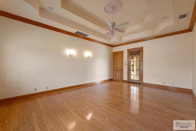 empty room with ceiling fan, a raised ceiling, crown molding, and light hardwood / wood-style flooring