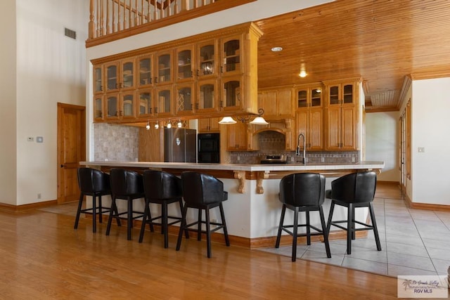 kitchen featuring a kitchen bar, stainless steel fridge, kitchen peninsula, tasteful backsplash, and light hardwood / wood-style floors