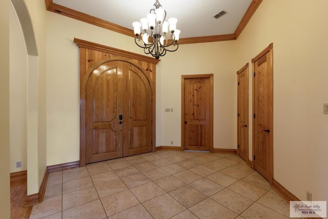 entryway with crown molding, light tile patterned floors, and an inviting chandelier