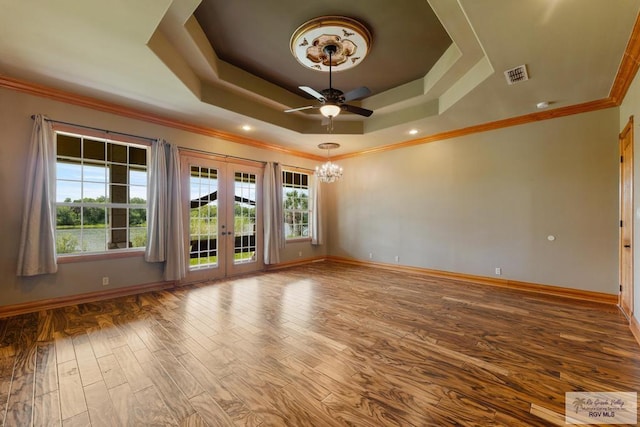 empty room featuring french doors, ceiling fan with notable chandelier, hardwood / wood-style flooring, ornamental molding, and a tray ceiling