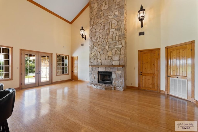 unfurnished living room featuring french doors, a stone fireplace, high vaulted ceiling, crown molding, and light hardwood / wood-style floors