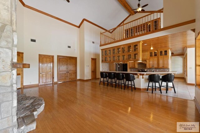 living room with ceiling fan, beam ceiling, high vaulted ceiling, a fireplace, and light hardwood / wood-style floors