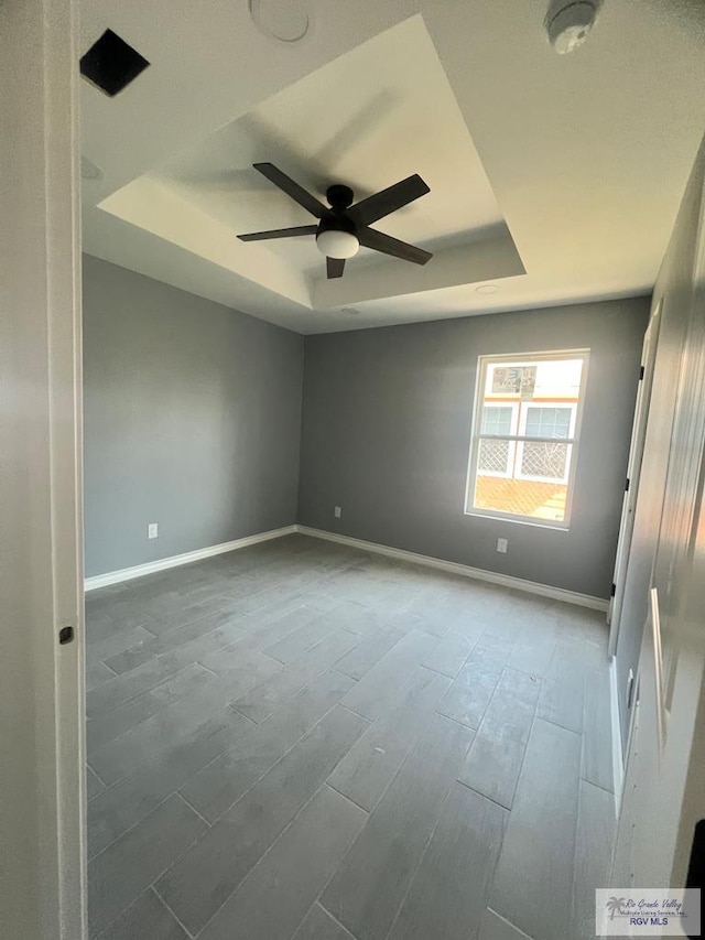 unfurnished room with baseboards, ceiling fan, wood finished floors, and a tray ceiling