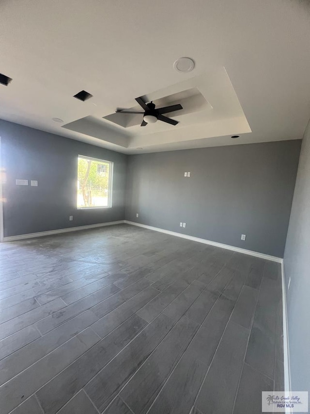 unfurnished room with baseboards, dark wood-type flooring, ceiling fan, and a tray ceiling