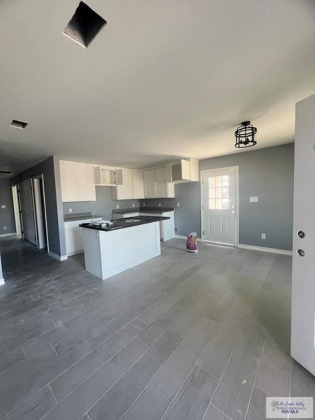 kitchen with a kitchen island, dark countertops, baseboards, wood tiled floor, and white cabinetry