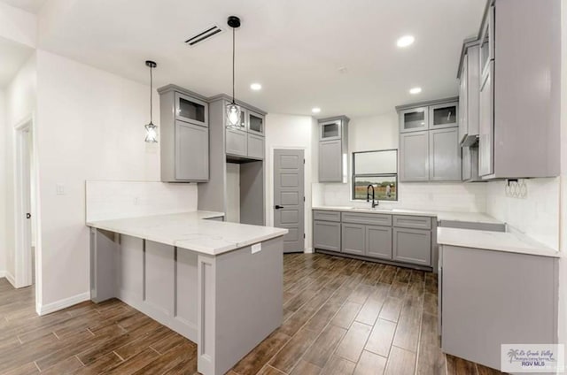 kitchen with light stone countertops, sink, hanging light fixtures, dark hardwood / wood-style flooring, and kitchen peninsula