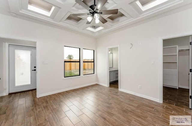 unfurnished bedroom featuring a walk in closet, ensuite bath, coffered ceiling, and hardwood / wood-style flooring